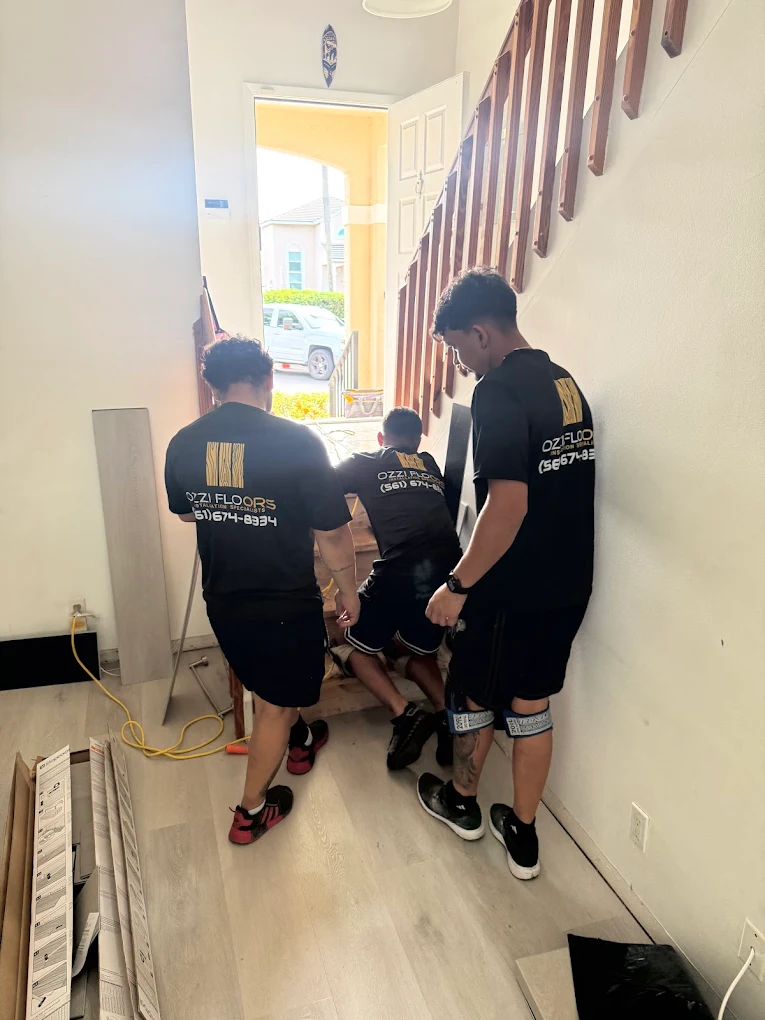 Three Ozzifloors installers carrying material in through the front door of a house, boxes of plank stacked against the wall