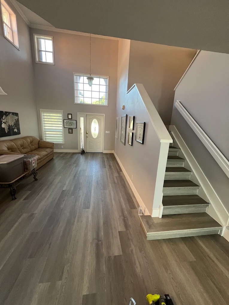 A finished grey-brown plank floor in a two-storey entry, with the staircase wrapped in matching plank treads