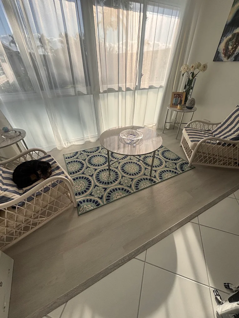 A sunlit sitting room where a new floor meets the existing white tile at a step