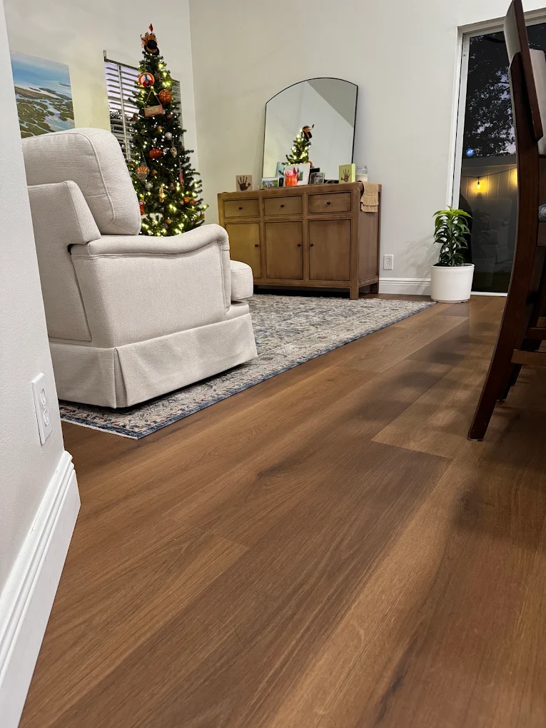 Warm wide-plank flooring installed by Ozzifloors in a living room, running past an armchair and a rug